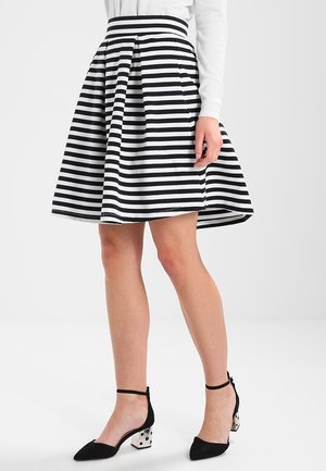 Černo-bíle pruhovaná A-linie sukně s vysokým pasem, sklady a hladkou texturou. V kombinaci s černými lodičkami na kotníkovém pásku.