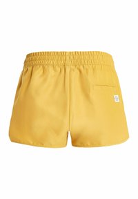 Geel short gemaakt van lichtgewicht stof met een elastische tailleband, een achterzak en een klein logo标签 aan de achterkant.