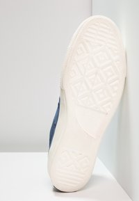 Baskets bleu marine avec semelle en caoutchouc, présentant une semelle inférieure texturée et à motifs ainsi que le logo classique Converse sur le côté.