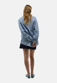 Chemise rayée bleue et blanche à manches longues, associée à un short en denim foncé et des ballerines bleues, vue de dos.