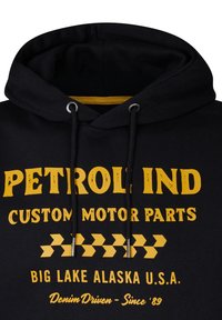 Zwarte hoodie met gele tekst en graphics. Beschikt over een trekkoord in de capuchon, een zachte textuur en een gedurfd ontwerp met de tekst "Petrol Ind Custom Motor Parts."