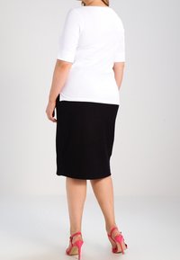 Valkoinen istuva toppi, jossa on lyhyet hihat, yhdistetty mustaan, ribbineulottuun polvipituiseen hameeseen. Asun täydentävät vaaleanpunaiset korkokantasandaalit.