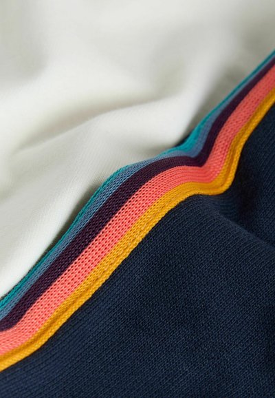 Gros plan sur des plis de tissu montrant un motif tricoté à rayures bleu marine, blanc et multicolore avec des bords turquoise, violet, corail et jaune.