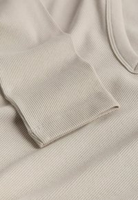 Tessuto a coste beige con superficie testurizzata e maniche arrotolate. Il materiale presenta sottili linee orizzontali, creando un aspetto morbido e accogliente.