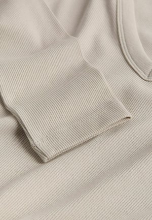 Béžová ribbovaná tkanina s texturovaným povrchem a ohrnutým rukávem. Materiál vykazuje jemné horizontální pruhy, což vytváří měkký a útulný vzhled.
