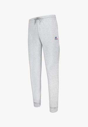 Pantalones de chándal grises hechos de una tela suave, con una cintura con cordón, piernas ajustadas y un pequeño logo en azul y rojo en el lado izquierdo.