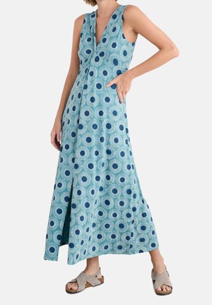 Vestido maxi azul sin mangas con patrones de rayos de sol en azul oscuro, escote en V, bolsillos laterales, combinado con sandalias cuña gris claro.