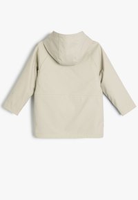 Beige vattentät jacka med huva, lång ärm och rak passform. Slät textur utan synliga mönster eller hårdvarudetaljer.