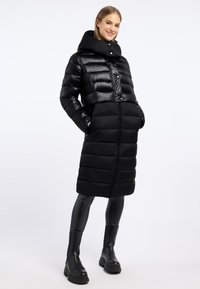 Czarna kurtka puchowa z wysokim kołnierzem, pikowanym wzorem, zapięciem na guziki z przodu oraz bocznymi kieszeniami. Modelka nosi czarne legginsy i botki za kolano.
