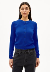 Blauer Strickcardigan mit Rundhalsausschnitt, langen Ärmeln und vorderen Knöpfen. Der Stoff hat eine glatte Textur und wird mit dunkelgrauen, hoch taillierten Jeans kombiniert.