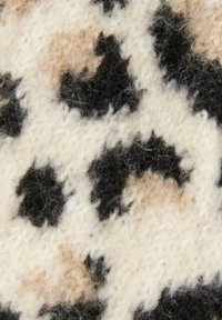 Primo piano di un tessuto morbido e peloso con macchie irregolari nere e beige su uno sfondo bianco crema, che ricorda un motivo animalier.