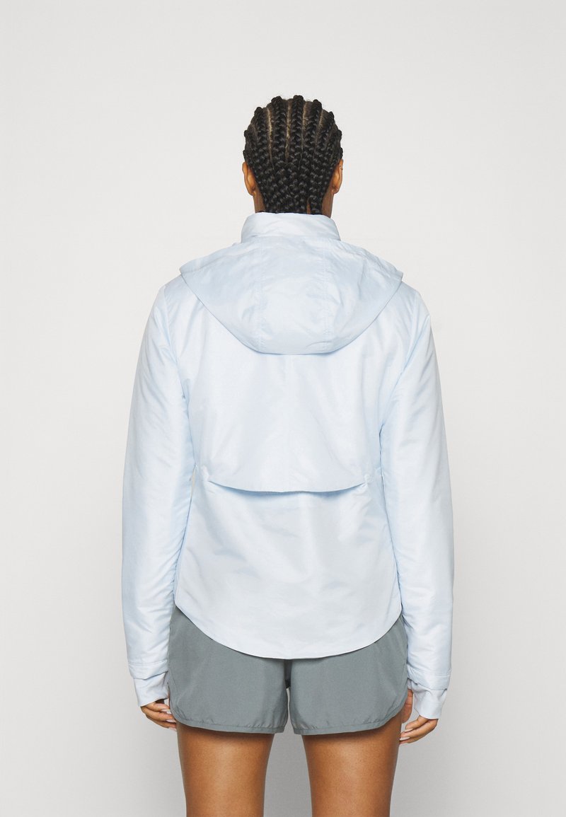 Himmelblau, leichte Jacke mit Kapuze, mit einem Rückenbelüftungsdesign. Kombiniert mit grauen Shorts, glatter Textur und lässiger Passform.