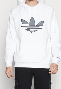 Vit hoodie med kängurufickor och dragsko, med en grå Adidas-logotyp på framsidan och ribbade ärmslut.
