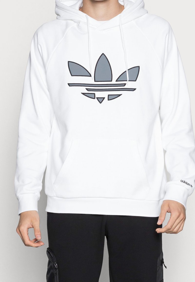 Vit hoodie med kängurufickor och dragsko, med en grå Adidas-logotyp på framsidan och ribbade ärmslut.