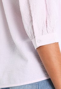 Vaaleanpunainen raidallinen paita, jossa on teksturoitu kangas ja puffi-hihat, nappikoristeet hihoissa sekä rento istuvuus.