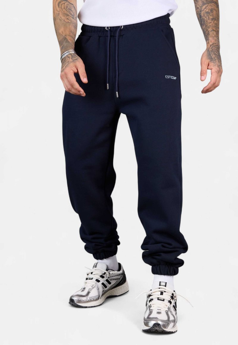 Dunkelblaue Sweatpants mit elastischen Bündchen, Kordelzugbund und Seitentaschen; mit einem kleinen weißen Logo auf der linken Seite.