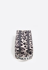 Mochila de estampado de leopardo que presenta dos cremalleras negras paralelas y una correa blanca con texto negro de marca en la base. La tela tiene una textura suave.