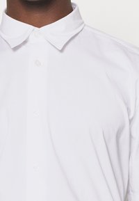 Camisa blanca de botones con cuello extendido, hecha de suave tela de algodón, con una textura lisa y cierre de botones claro.