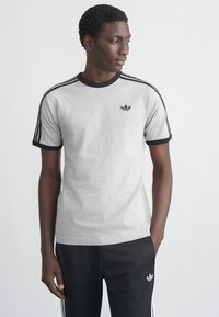 Γκρι βαμβακερό μπλουζάκι με μαύρο ριμπ γιακά και μανσέτες στα μανίκια. Διαθέτει τρεις μαύρες ρίγες στους ώμους και μικρό μαύρο λογότυπο στο στήθος.