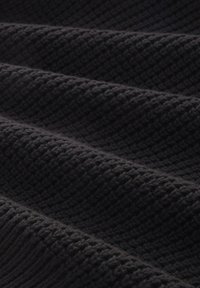 Černá pletená látka s texturovaným povrchem, která má tkaný vzor a jemné záhyby, ukazující hloubku a měkkost.