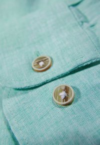 Tessuto verde chiaro con trama e due bottoni rotondi col colore crema che presentano un motivo orizzontale e dettagli in filo bianco.