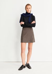 Zwarte lange mouwen top, bruine corduroy rok met zijzakken, en zwarte loafers met studaccenten. Sjaal om de nek gedrapeerd.