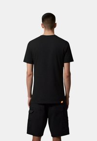 T-shirt nero a maniche corte con un design testurizzato, dotato di collo a giro e un'etichetta arancione a contrasto in fondo, indossato con pantaloni cargo neri.