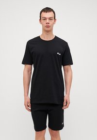 Juodas laisvalaikio T-shirt ir šortai, pagaminti iš minkštos medvilnės. T-shirt turi mažą baltą logotipą kairiajame krūtinės šone; šortai turi logotipą šone.