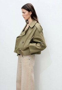 Olive green cropped jacket with double-breasted button closure, large lapels, and side pockets, paired with light beige wide-leg pants.