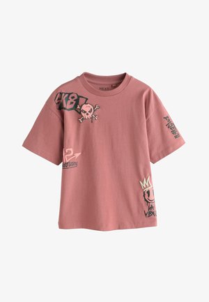 Pink T-shirt med korte ærmer med sort-hvid kranie, "SK8!", pile, smiley med krone og graffiti-stil tekstgrafik.