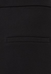 Zwart textiel met een gestructureerd oppervlak bevat een klein, rechthoekig zakje dat in het ontwerp is genaaid. Eenvoudige stikseldetails zijn zichtbaar.