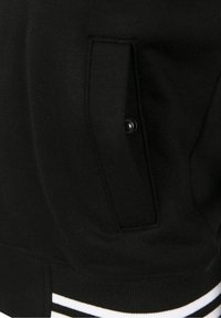 Sweat-shirt noir avec une poche latérale munie d'un bouton en métal, ourlet côtelé avec des rayures blanches et bleues en bas, texture de tissu doux.