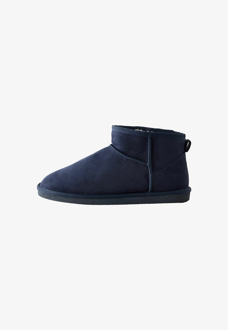 Chausson en cuir suede bleu marine avec doublure en peluche, semelle plate et boucle à l'arrière pour un enfilage facile, vu de côté.