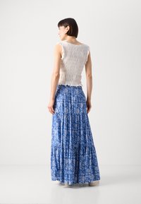 Weißes, gesmoktes Oberteil mit Rüschensaum, kombiniert mit einem blauen, floral gemusterten Maxirock mit Stufen und einer lässigen Silhouette.
