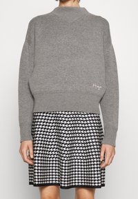 Szary dzianinowy sweter z wysokim dekoltem i prążkowanymi mankietami, w połączeniu z czarno-białą spódnicą w wzór houndstooth, wykończoną na dole.