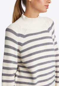 Strickpullover mit hohem Kragen, versehen mit cremefarbenen und grauen horizontalen Streifen, strukturiertem Rippmuster und einem lässigen Schnitt.