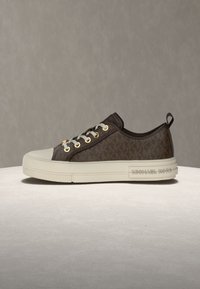 Brauner Stoff-Sneaker mit cremefarbenem Gummi-Zehenkappe und Sohle, goldenen Ösen und einem strukturierten Design. Mit einem Logo an der Seite.