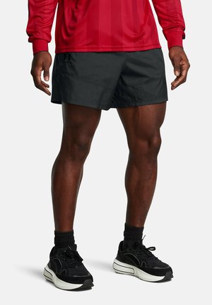 Pantaloni athletic neri con un design elegante, caratterizzati da una texture liscia e cuciture laterali, abbinati a sneakers nere e calze a righe nere.