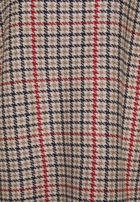 Uldstof med et houndstooth mønster i beige, sort og rød med et rutenet-layout, der viser en struktureret, vævet overflade.