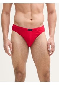 Culotte de bikini rouge en coton avec une taille basse, dotée d'une étiquette noire à la taille et d'un tissu lisse et extensible.