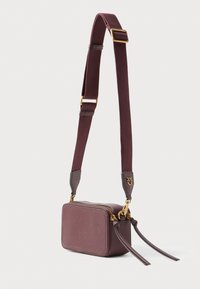 Bordo usnjeni crossbody nahrbtnik pravokotne oblike, zlata strojna oprema, nastavljiv trak in dve okrasni resici. Zadrga za zapiranje.