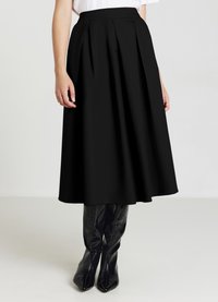 Gonna nera plissettata realizzata in un tessuto morbido, che arriva a metà polpaccio. Abbinata a stivali neri lucidi al ginocchio.