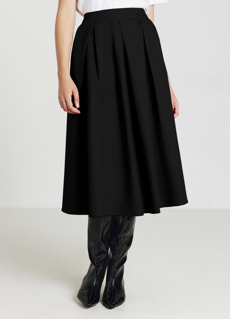 Gonna nera plissettata realizzata in un tessuto morbido, che arriva a metà polpaccio. Abbinata a stivali neri lucidi al ginocchio.