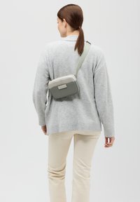 Borsa a tracolla grigia chiara con una forma rettangolare strutturata, realizzata in un materiale liscio, con una parte superiore beige a contrasto e hardware opaco.