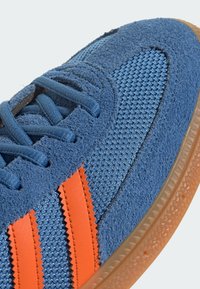 Blue sneaker made of textured mesh and suede, featuring orange zigzag stripes and a gum rubber sole with a patterned tread.