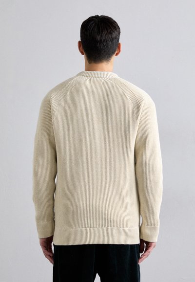 Cream-colored ribbed knit sweater with long sleeves, crew neck, and a relaxed fit. Visible textured pattern on the fabric.