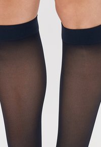 Čierne priesvitné pančuchy po stehná s hladkou textúrou, s hrubým nepriehľadným pásom na vrchu pre lepšie držanie a oporu.