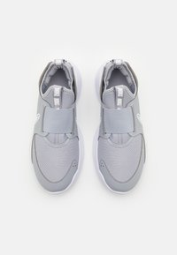 Pari harmaat Nike-vetoketjulliset lenkkarit leveillä velcro-nauhoilla, verkkokankaisilla yläosilla ja valkoisilla pohjilla, kuvattuna ylhäältä valkoista taustaa vasten.