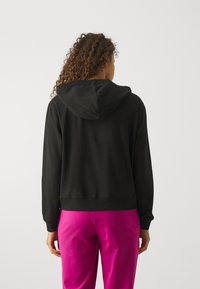 Zwarte cropped hoodie met een trekkoordcapuchon en lange mouwen, met een zachte textuur en een rechte zoom. Gecombineerd met felroze broek.