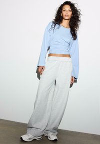 Maglia a maniche lunghe azzurro chiaro abbinata a pantaloni della tuta grigi e larghi. L'outfit presenta una vestibilità comoda e una texture simile al cotone. Indossato con sneakers bianche.